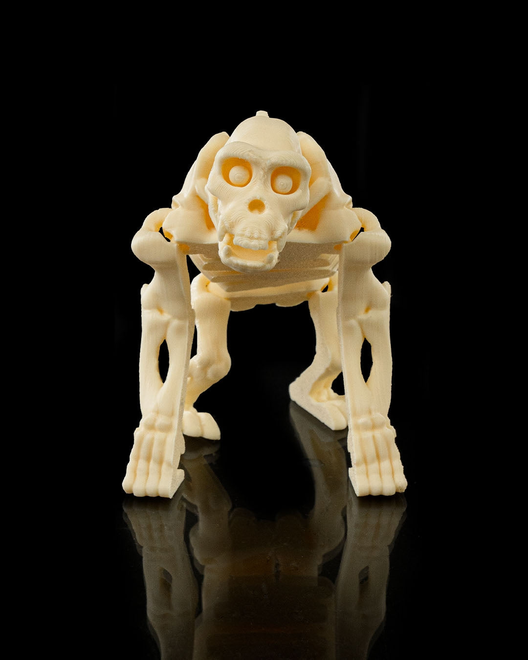Front view of 3D printed Flexi Skeleton Chimp, articulated fidget toy standing on black reflective surface.