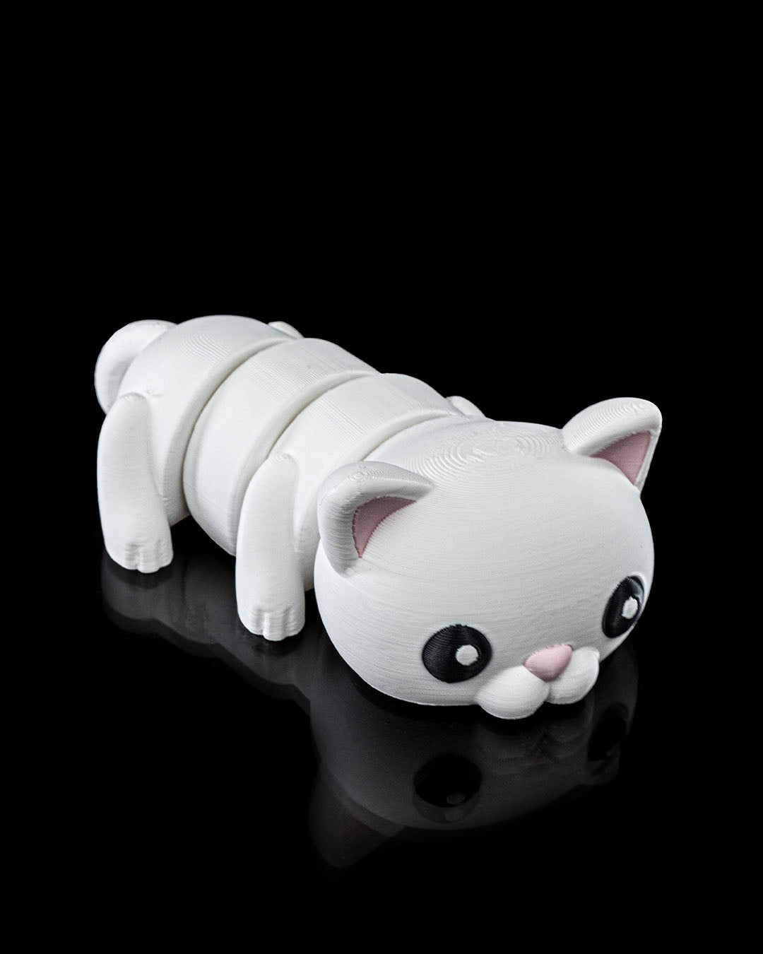 Angled view of a 3D printed Flexi Cat articulated toy with white body and pink ears, lying on a reflective black surface.