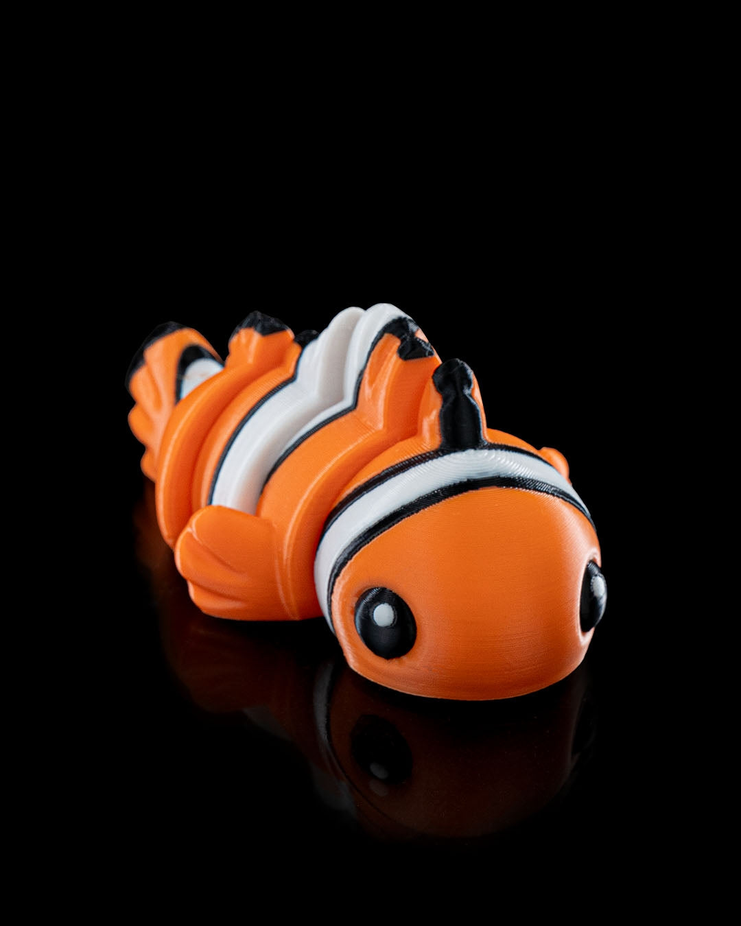 Angled view of a 3D printed flexi clownfish with bright orange, white, and black stripes.