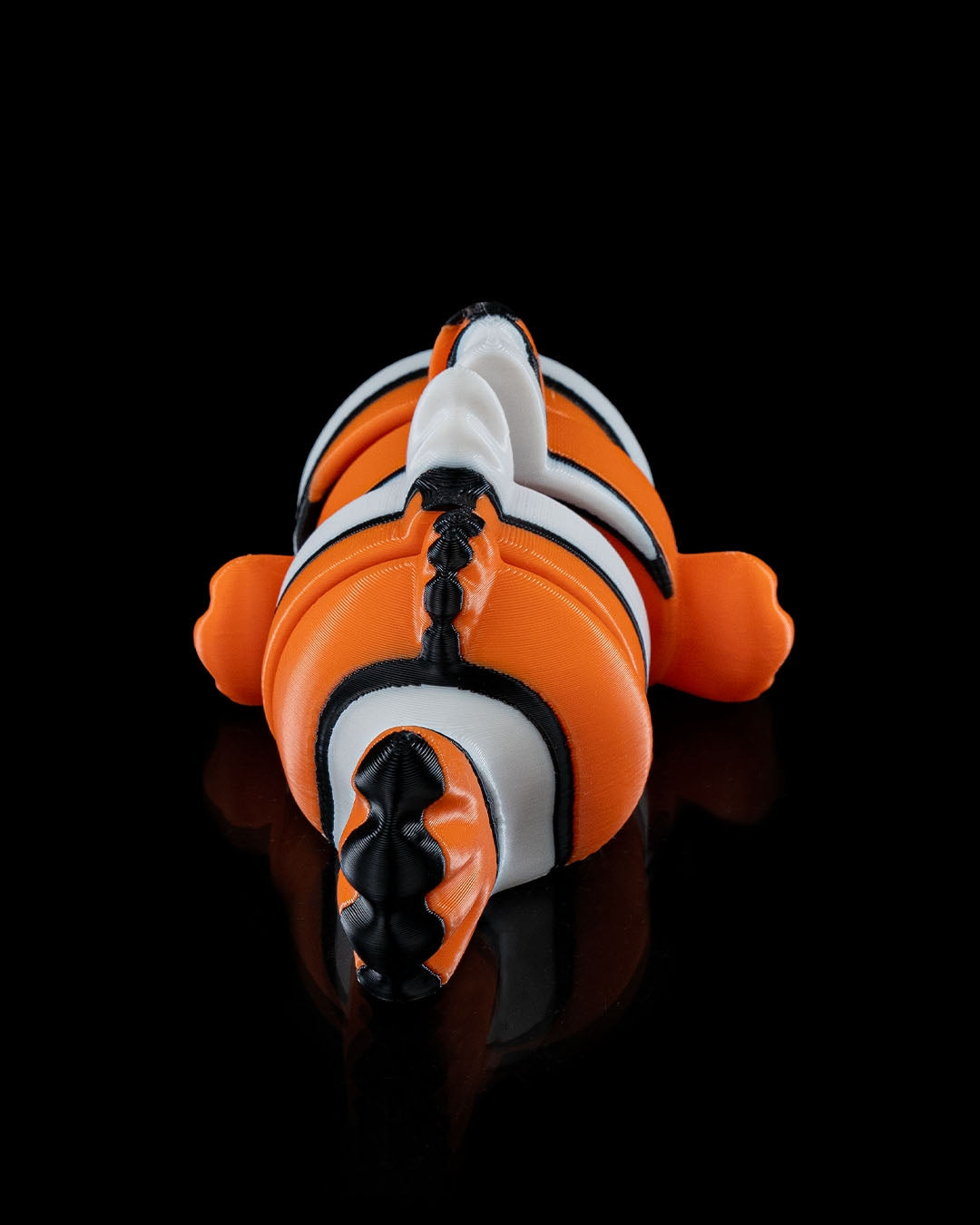 Rear view of a 3D printed flexi clownfish with bright orange, white, and black stripes.