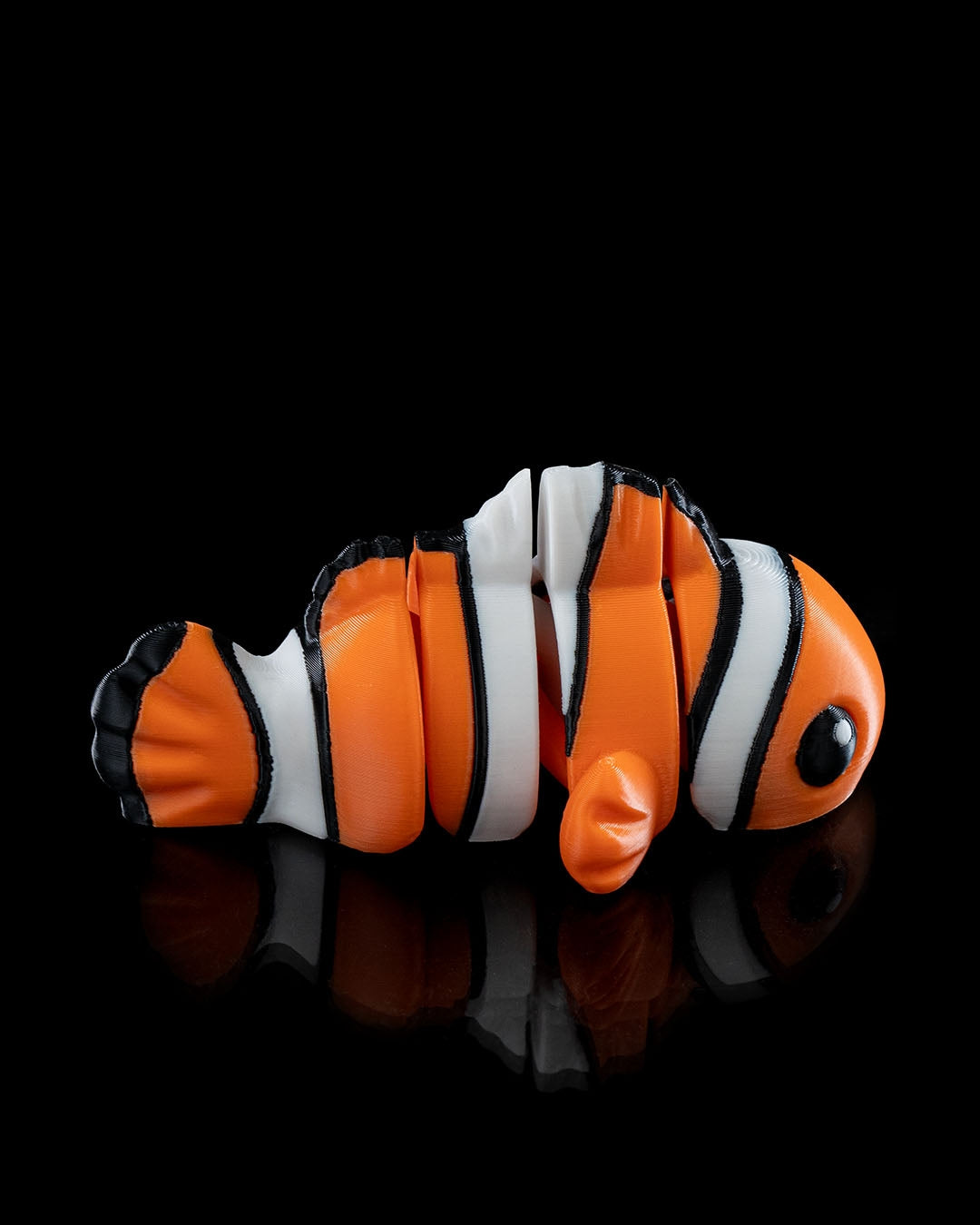 Side view of a 3D printed flexi clownfish with bright orange, white, and black stripes.