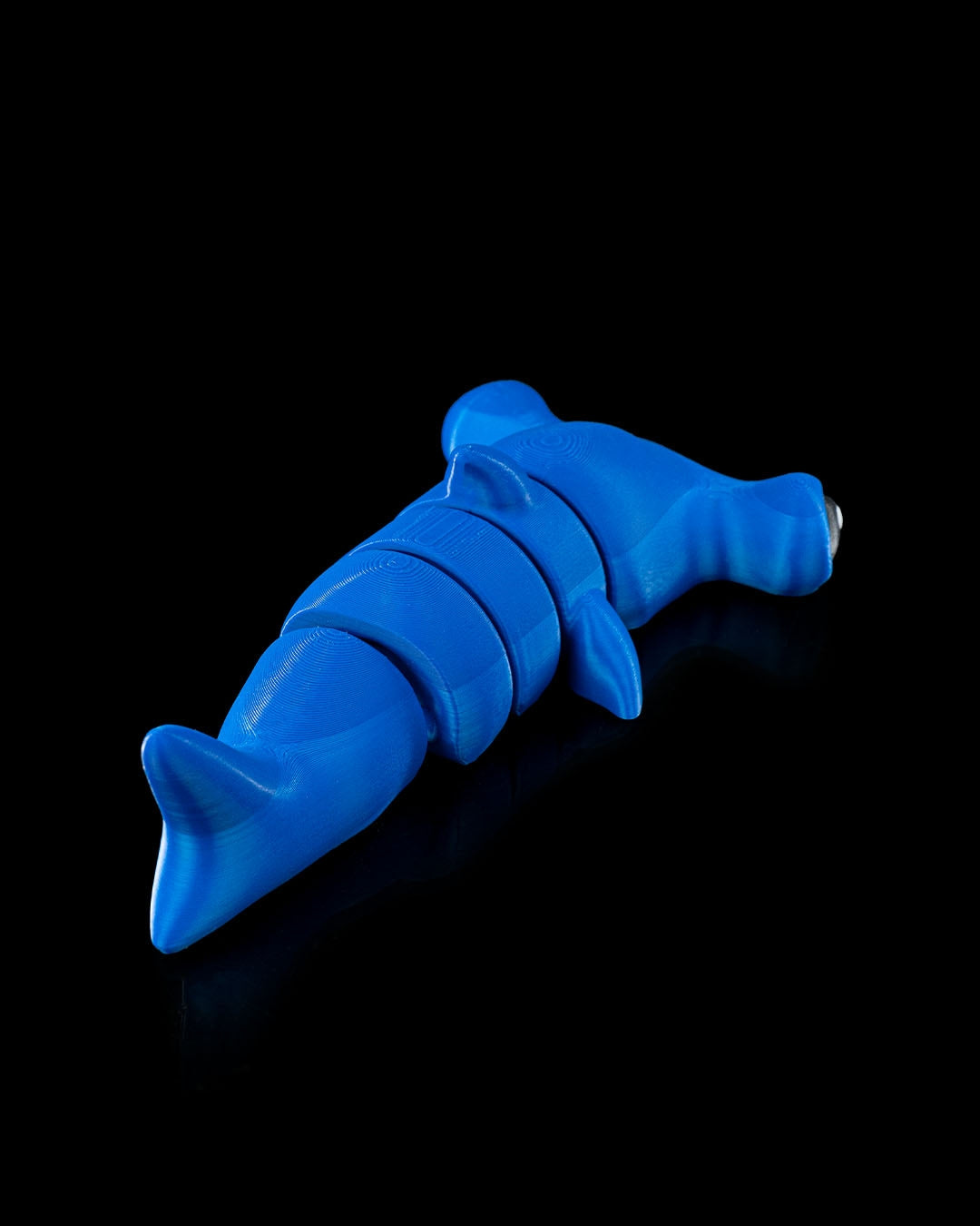 Rear view of 3D printed blue flexi hammerhead shark toy shown on black background with articulated segments.