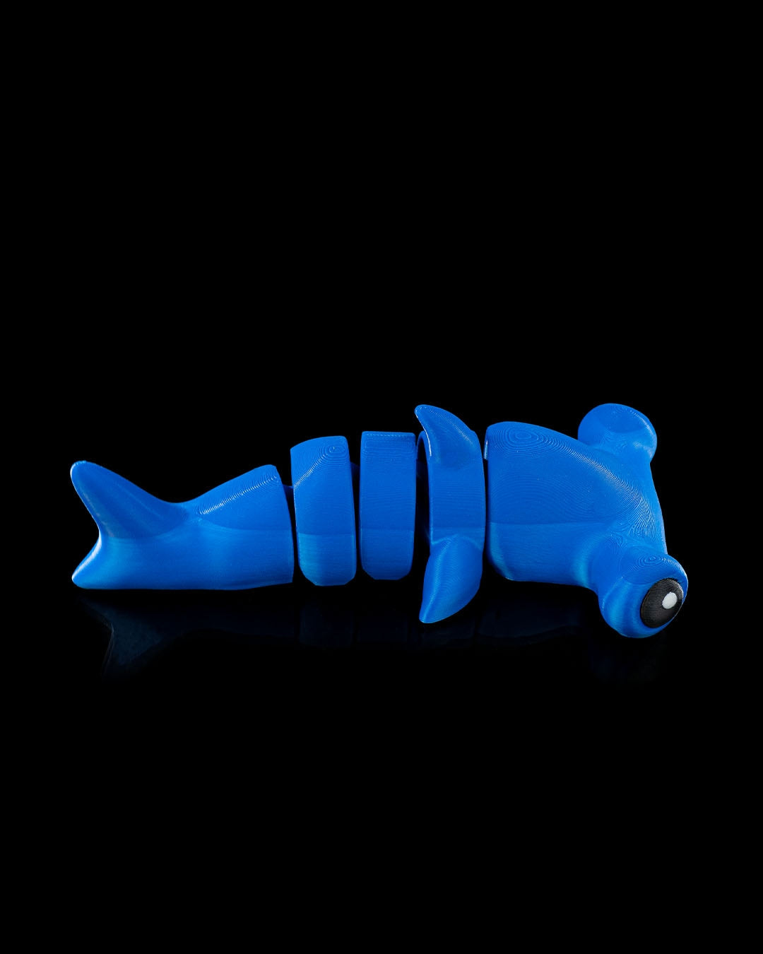 Side view of 3D printed blue flexi hammerhead shark toy shown on black background with articulated segments.