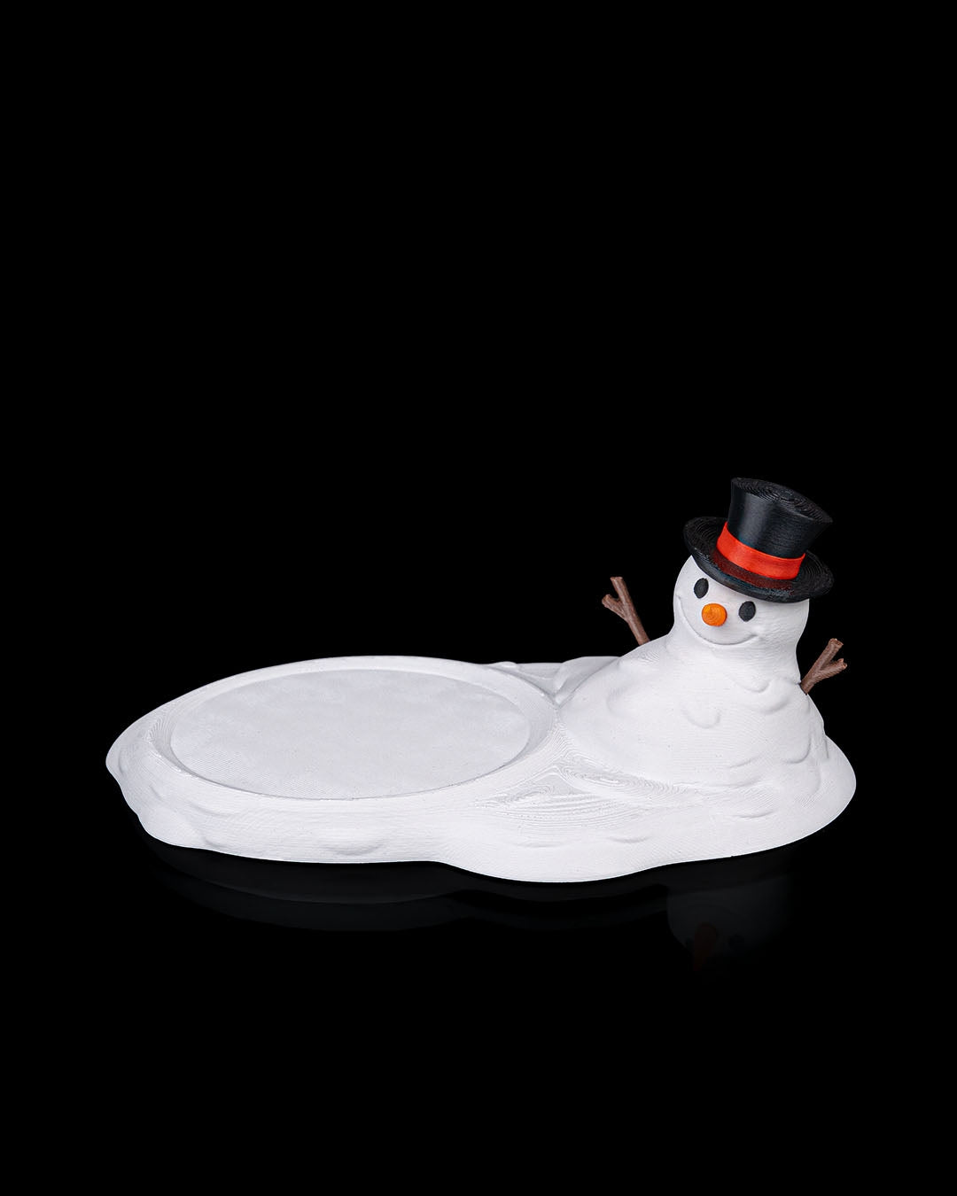 3D printed Meltproof Snowman Coaster with top hat and carrot nose beside a mug on white snow-like base.