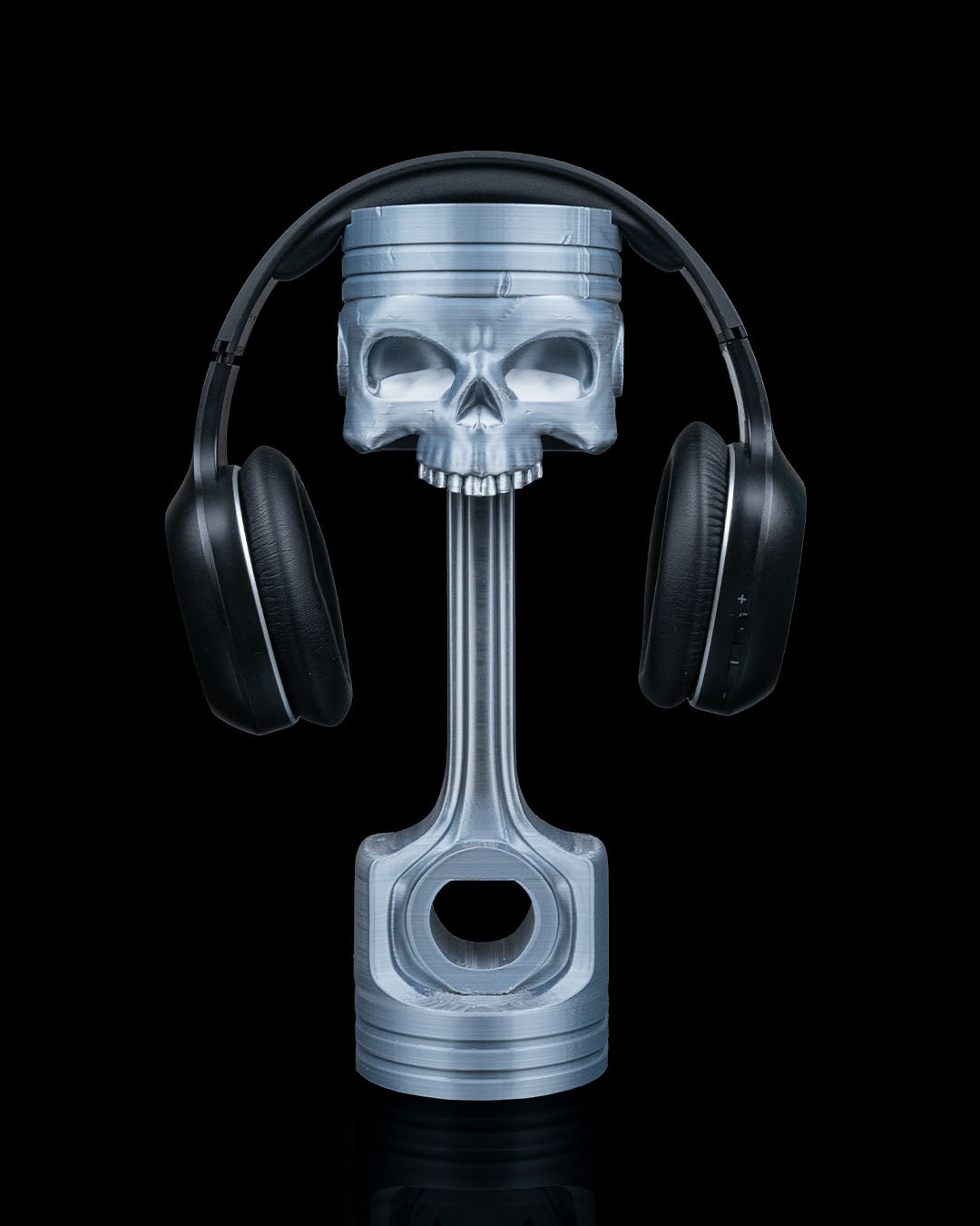 3D printed Piston Skull Headphone Holder in metallic silver holding headphones.