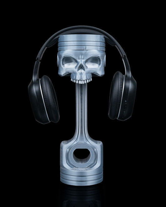 3D printed Piston Skull Headphone Holder in metallic silver holding headphones.
